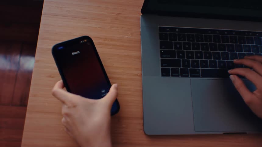 Hands and fingers of a teenage girl typing on the keyboard of a laptop computer as she stops to look at her phone