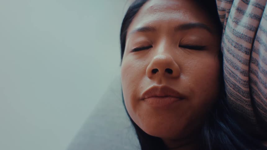 An asian woman laying on her side slowly closes her eyes and sleeps