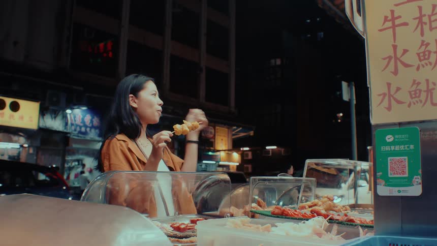 A woman enjoys street food at a night stall and gives a thumbs up
