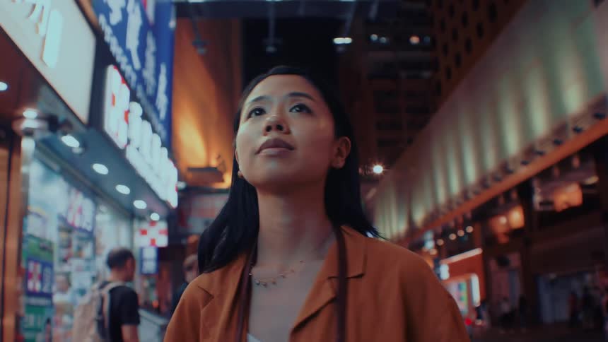 Young woman on a downtown street at night turns around as she walks looking at buildings