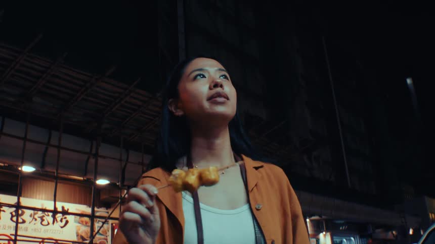 A woman samples street food while exploring a bustling night market outdoors