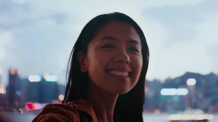 Young woman smiles as she stands with buildings in the distance