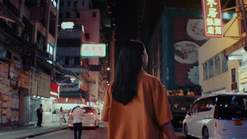 Young woman walks on a downtown street among other people at night as she stops to take a picture with her camera
