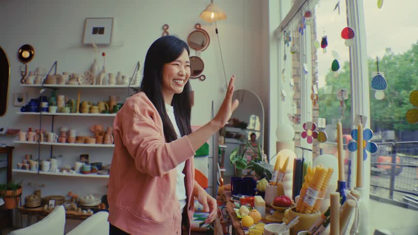 Female shop owner is waving goodbye with a happy expression