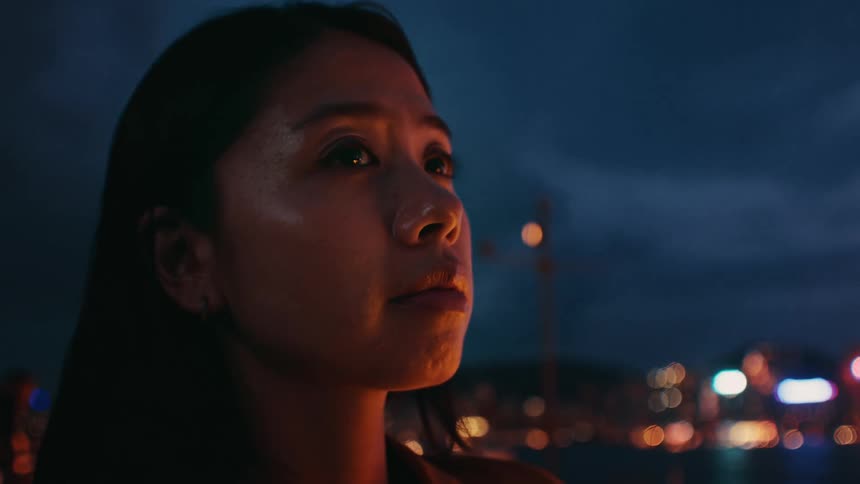 The woman stands by the water near the city at night