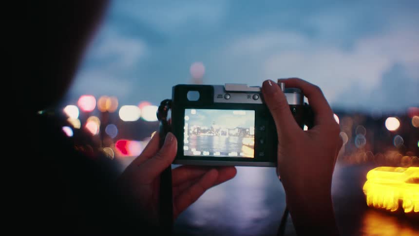 A photographer holds a digital camera against a backdrop of shimmering city lights the bright screen sharply displaying the illuminated skyline