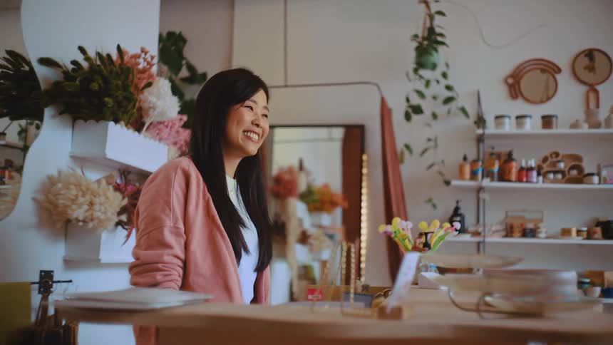 Man stands at the counter of a retail store as the woman hands him his shopping bag and they shake hands