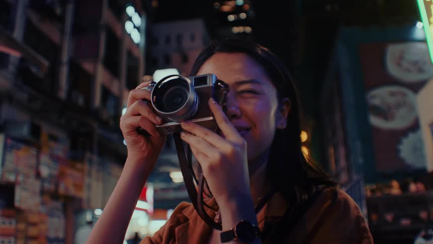 The woman smiles while taking pictures of the buildings at night