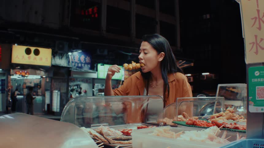 Woman eats street food at a night market stall with displayed food cases