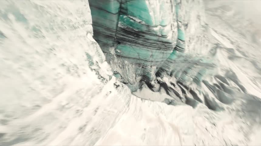 Snowcovered glacier shows fissures and a turquoise water flow between ice formations
