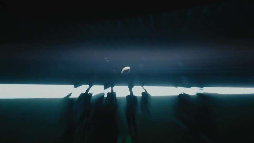 People standing around a football ball hanging in the air in an empty stadium