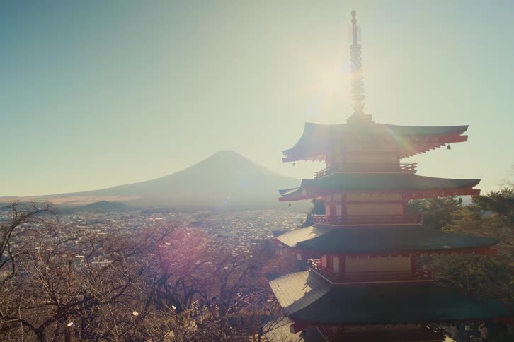Japanese pagoda lit by sunlight with mount fuji in the background and city below the mountain