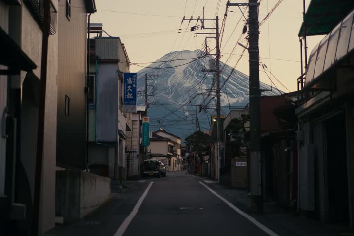 Narrow residential street leads toward mount fuji in the background between houses and power lines