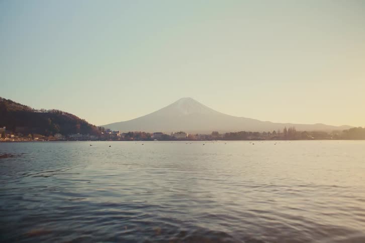 Mount fuji appears in the distance beyond a wide lake with gentle ripples under a clear sky