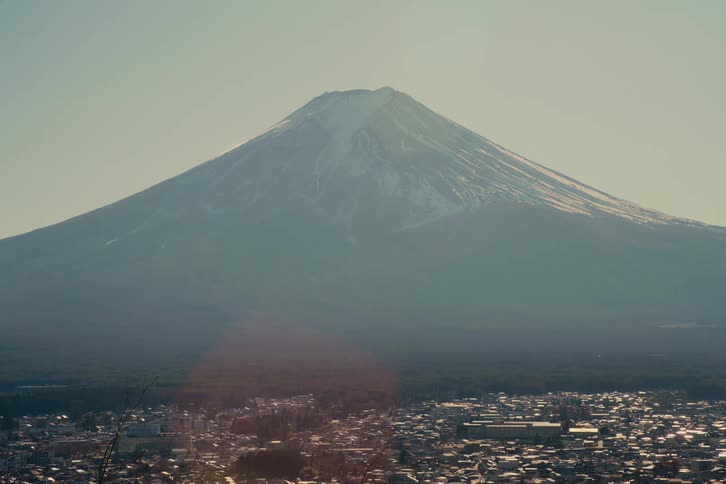 A snowy mount fuji towers over the nearby town on a foggy day