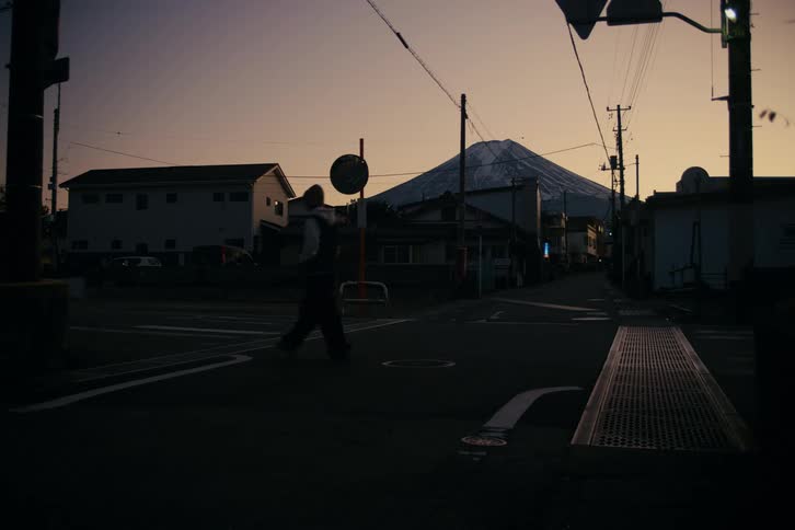 Woman walks through an intersection while red tints the sky