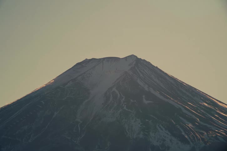 The rugged snowdusted summit of mount fuji is captured in a stunningly detailed closeup revealing the intricate textures of its volcanic crater and rocky ridges bathed in the soft golden light of a clear evening sky