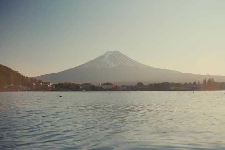 Mount fuji rises in the background beyond a lake with a gently rippled surface under a clear sky