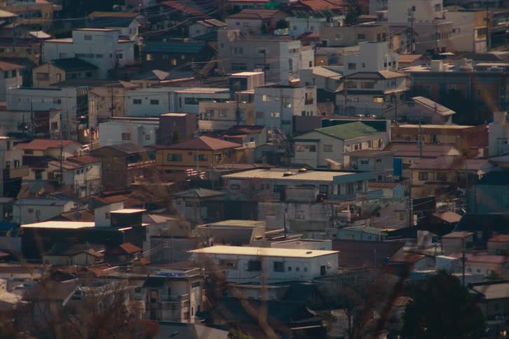 A densely populated hillside residential area with various houses and apartment buildings packed closely together under warm afternoon sunlight