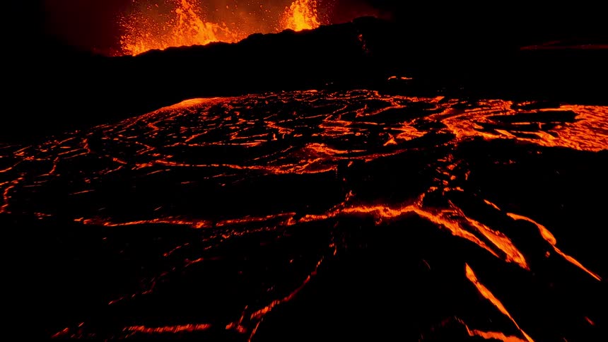 A volcanic eruption at night with bright lava flowing down the mountains slopes glowing against the dark sky