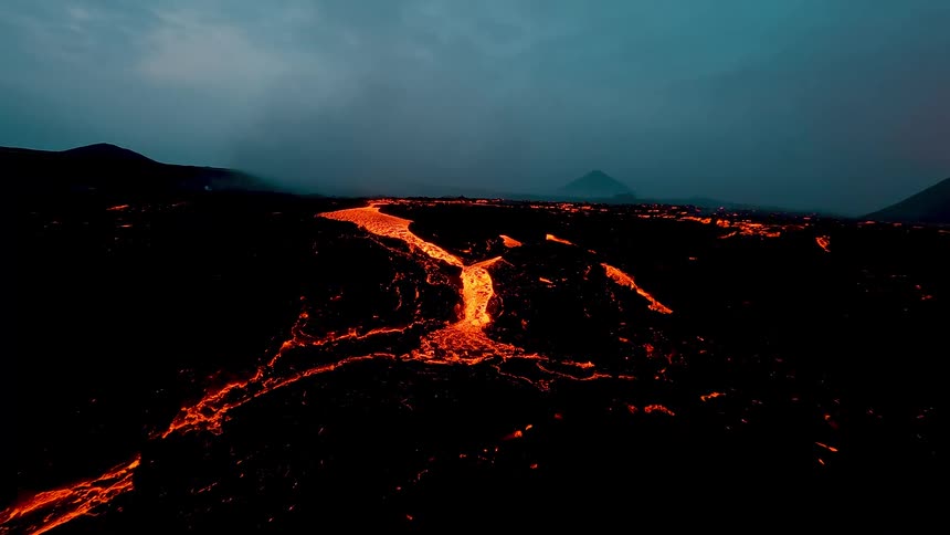 Glowing river of lava flows across volcanic terrain under a cloudy dusk sky