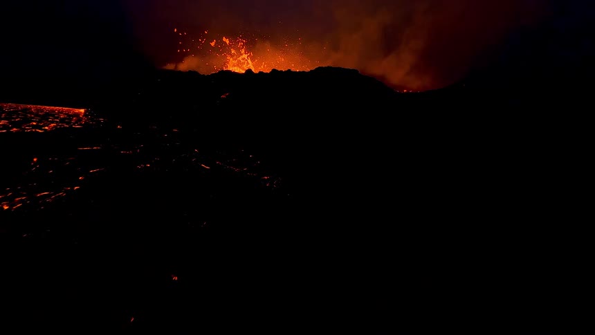 A glowing river of molten lava flows through a dark volcanic landscape at night