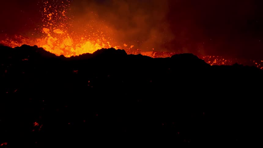 Molten hot lava flies into the air splashing and flowing down the side of an erupting volcano