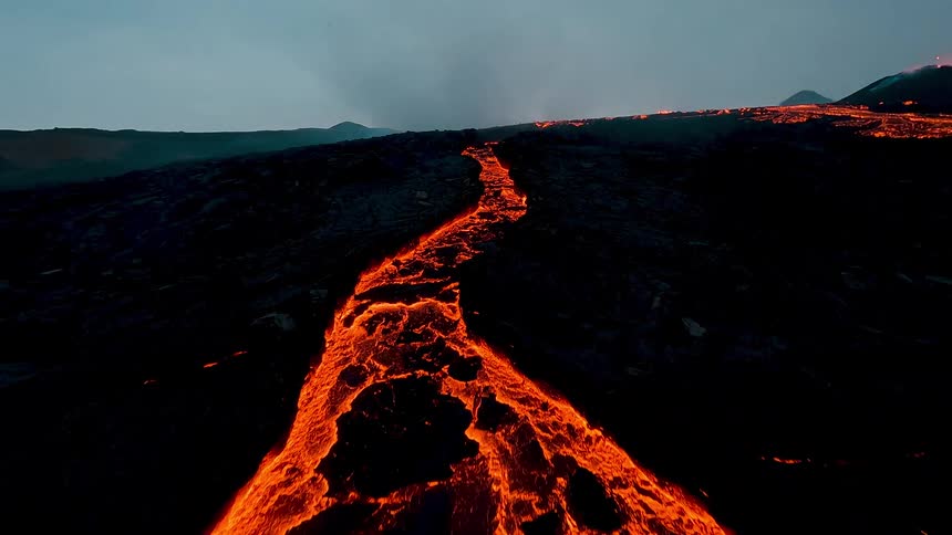 Lava flowing down a mountain after a volcanic eruption at sunset glowing brightly against the warm fading light