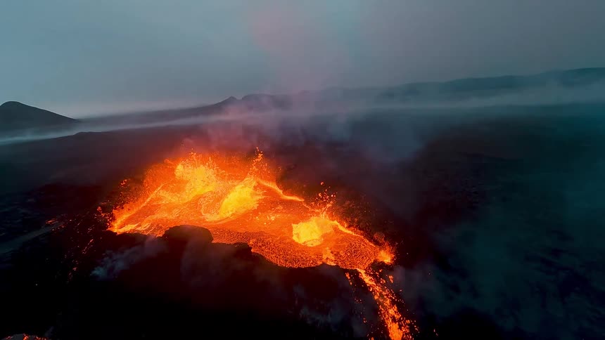 Molten hot lava flies into the air splashing and flowing down the side of an erupting volcano