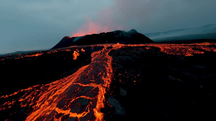 Glowing lava flows converge across dark volcanic terrain under a cloudy sky