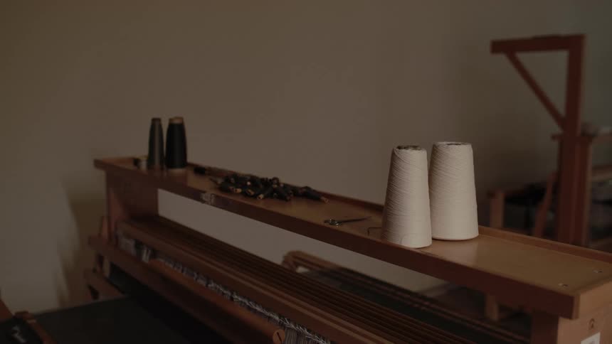 A weaving machine inside a warehouse with multiple threads stretched across the top ready for fabric production
