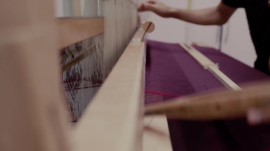 Purple fabric is woven on a wooden loom with tensioned threads during a handmade process