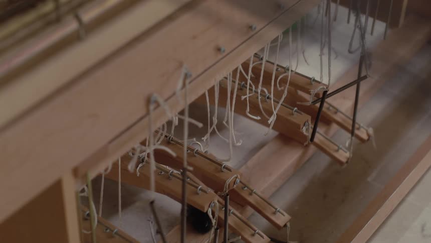 Underside view of loom with wooden treadles connected to cords and metal rods