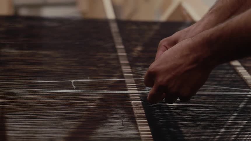 Hands adjust dark threads on a loom during fabric alignment
