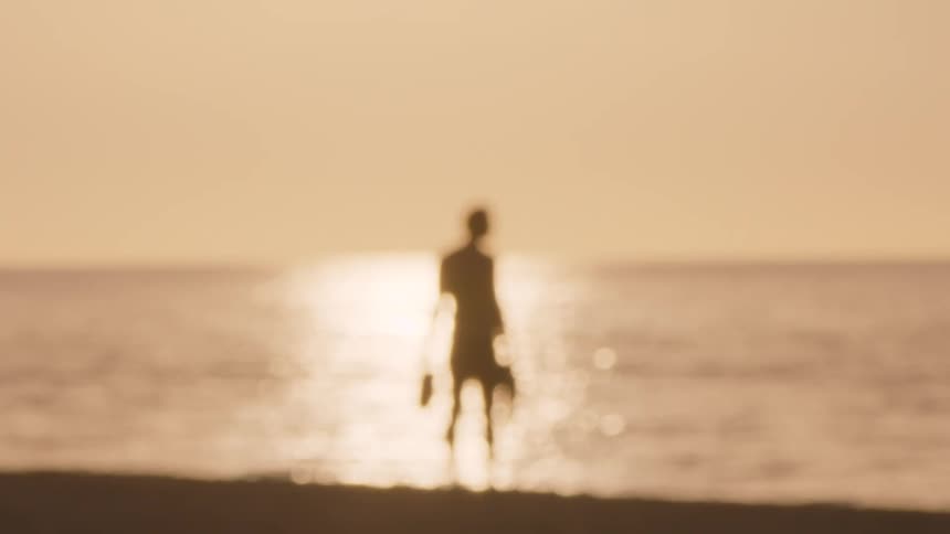 A blurry shot comes into focus revealing a mans silhouette against a beach sunset