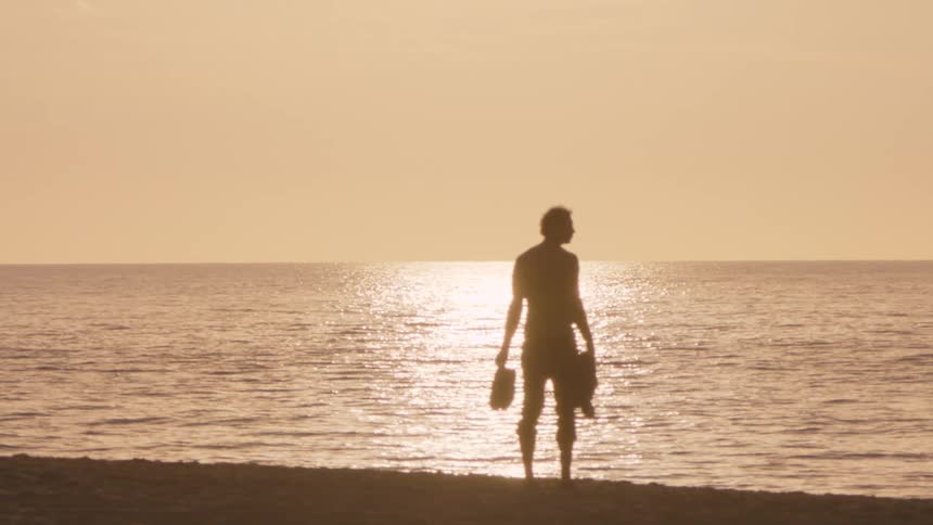 Man stands silhouetted against the sun while on the beach