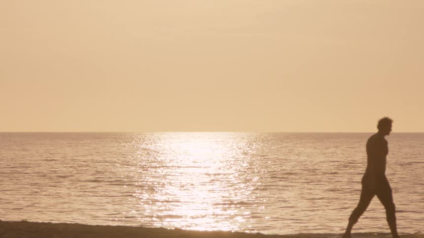 Man walking on the beach as the sun shines on the water