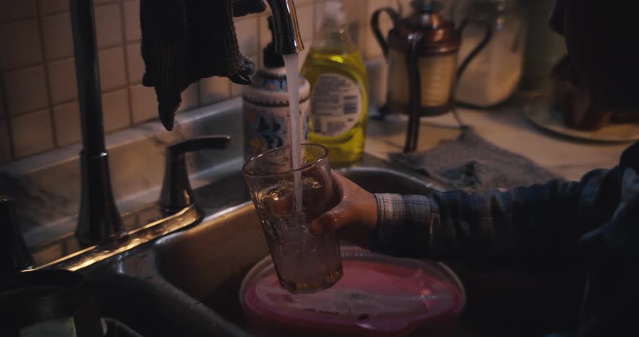 A person raising a glass cup beneath a kitchen tap then filling it with running water as it flows smoothly into the glass