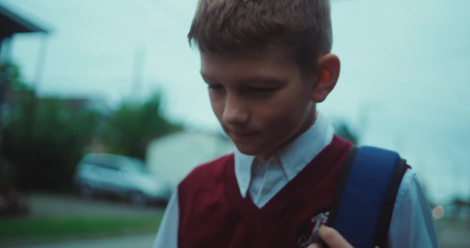 Boy walking on a neighborhood sidewalk holding his book bag over his shoulder