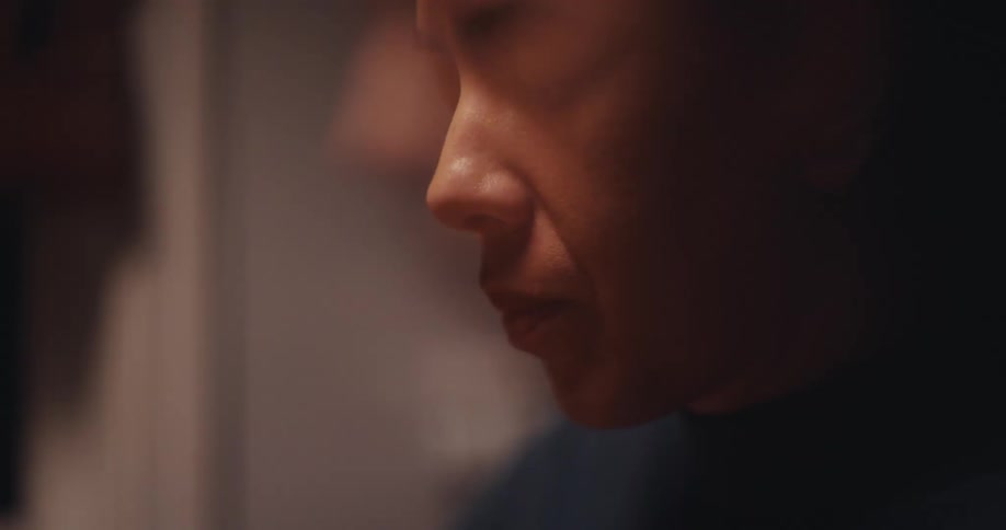 A woman is shown in a tight profile shot appearing to be in a moment of deep contemplation or prayershe keeps her eyes closed while slightly moving her lips set against a dark and softly lit background