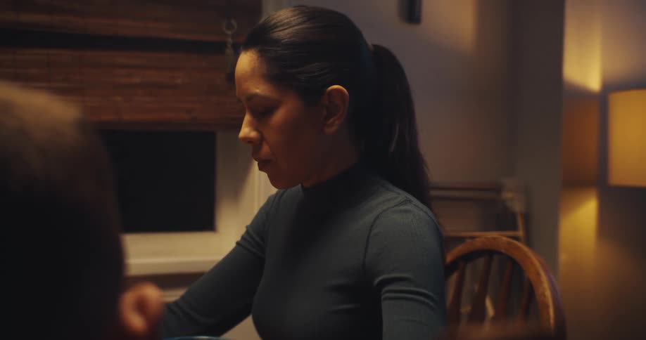 A young woman sitting at the dining table with her family bowing her head as she says a quiet prayer before dinner the warm light of the room creating a calm intimate atmosphere