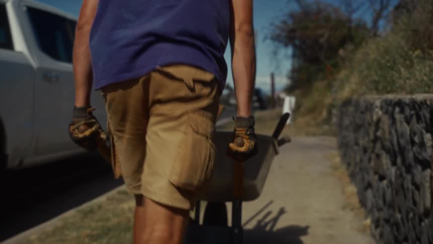 A young man pushing a wheelbarrow along the sidewalk under the bright sun