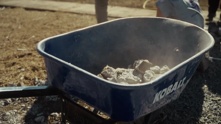 Three construction workers throwing rocks on a wheelbarrow outdoors during day time