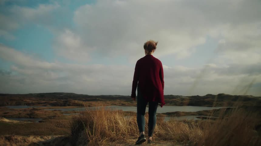 Woman in a red coat walking in a natural area with a lake in the background