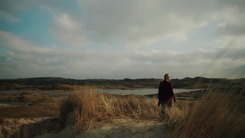 Woman in a red coat walks through the mountains with a lake in the background