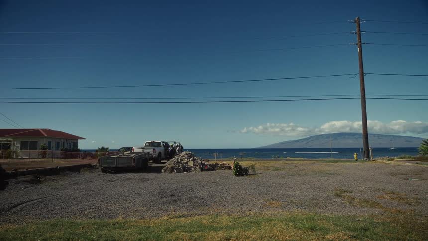 A pickup truck and trailer are parked in a gravel lot overlooking the ocean and a distant mountain island
