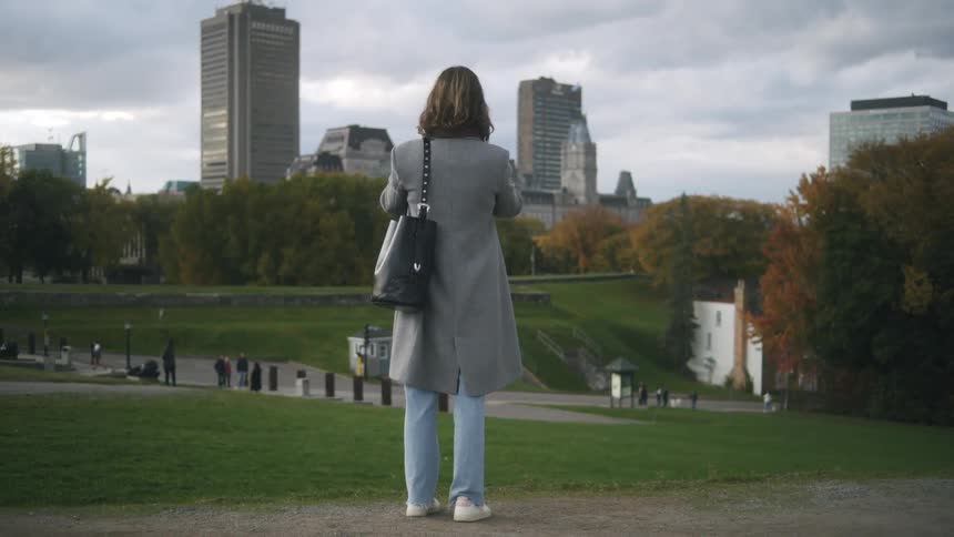 Back of a woman standing in a city park with people walking around at daytime