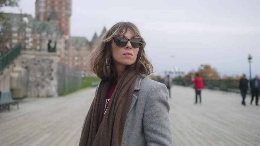 Woman wearing sunglasses and a scarf walking through a classic city