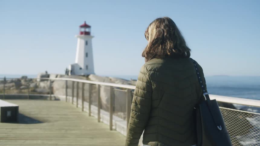 Woman with a green purse and jacket walking along a wooden deck
