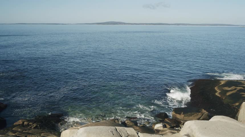 A rocky coastline with waves crashing against the shore at midday